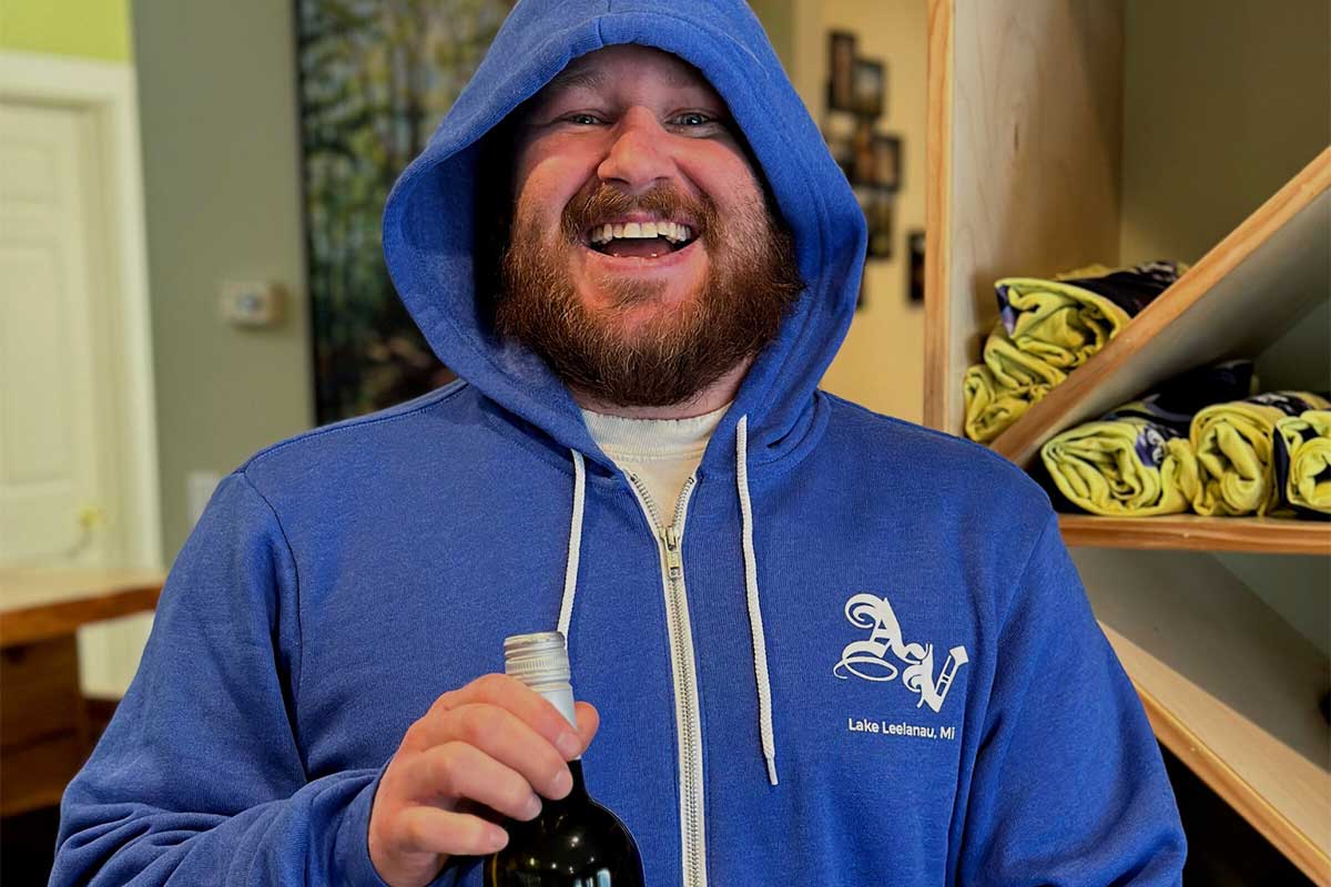 Man in a hoodie smiling holding a bottle of wine