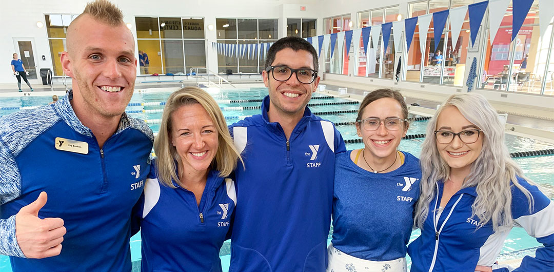 Smiling YMCA staff members huddled in front of pool